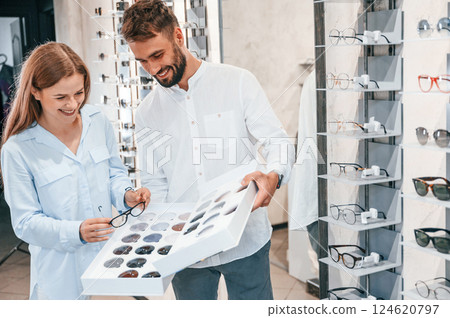 Standing and smiling. Man and woman in the glasses store. Helping to choose product 124620797
