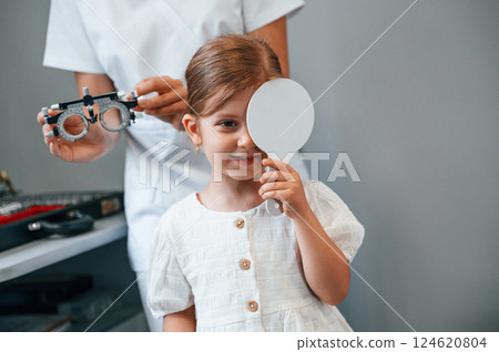Covering left eye. Little girl have their vision checking in the clinic by help of the female doctor Covering left eye. Little girl have their vision checking in the clinic by help of the female doctor 124620804