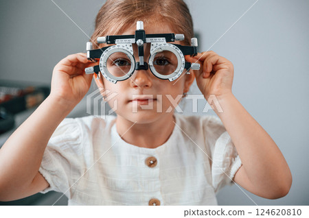 In special device with lenses. Little girl have their vision checking in the clinic by help of the female doctor In special device with lenses. Little girl have their vision checking in the clinic by help of the female doctor 124620810
