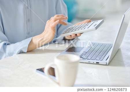 一位中年婦女在客廳一邊使用計算機一邊看著電腦 124620873