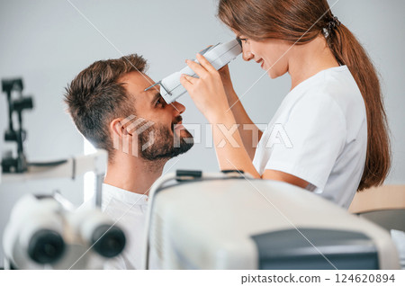 Modern technologies. Man's vision checked by female doctor in the clinic by using special optometrist device 124620894