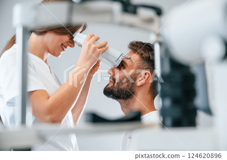 Side view. Man's vision checked by female doctor in the clinic by using special optometrist device Side view. Man's vision checked by female doctor in the clinic by using special optometrist device 124620896