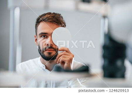 Covering right eye. Man is checking his vision indoors in the clinic 124620913
