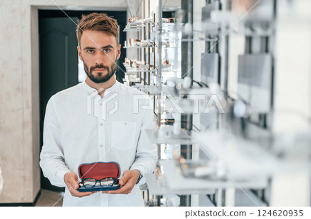 Holding case with eyewear. Stylish man with beard choosing glasses in the optics store Holding case with eyewear. Stylish man with beard choosing glasses in the optics store 124620935