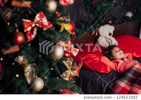 Little Curly Girl In Bedroom Near Christmas Tree With New Year Gifts Little Curly Girl In Bedroom Near Christmas Tree With New Year Gifts 124621082