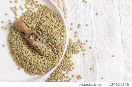 Plate full of dried raw green lentils with a wooden scoop on white table top view. Vegetarian food 124621226