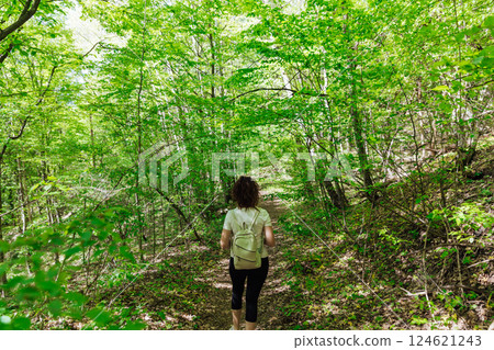 Female traveler walking along forest road in green mountain forest Female traveler walking along forest road in green mountain forest 124621243