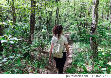 Female traveler walking along forest road in green mountain forest Female traveler walking along forest road in green mountain forest 124621245