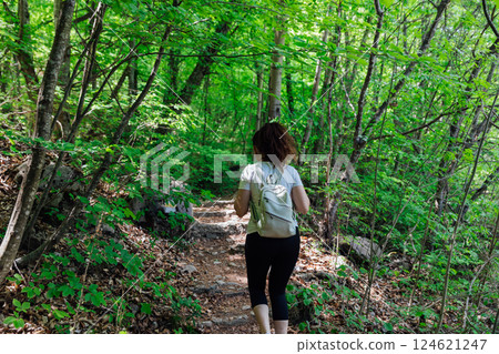 Female traveler walking along forest road in green mountain forest Female traveler walking along forest road in green mountain forest 124621247