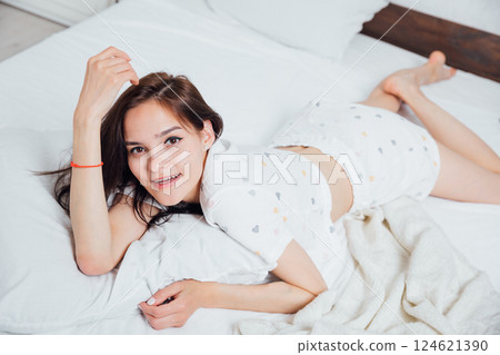 Beautiful woman in pajamas lying in bedroom on white bed Beautiful woman in pajamas lying in bedroom on white bed 124621390