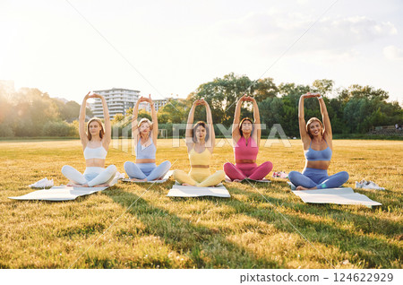 Doing yoga. Group of women have fitness outdoors on the field together 124622929
