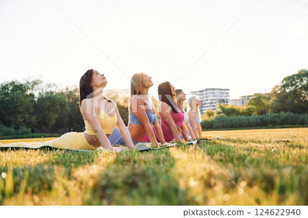 Doing yoga on the mats that on the grass. Group of women have fitness outdoors on the field together Doing yoga on the mats that on the grass. Group of women have fitness outdoors on the field together 124622940