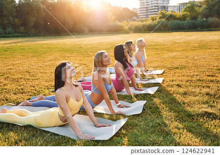Doing yoga on the mats that on the grass. Group of women have fitness outdoors on the field together Doing yoga on the mats that on the grass. Group of women have fitness outdoors on the field together 124622941
