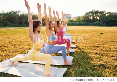 Doing warrior pose. Group of women have fitness outdoors on the field together Doing warrior pose. Group of women have fitness outdoors on the field together 124622951