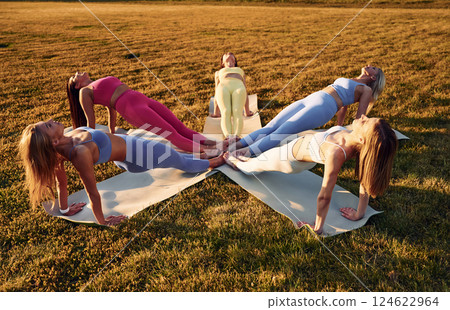 Doing upward plank. Group of women have fitness outdoors on the field together 124622964