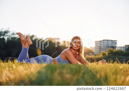 In blue clothes. Laying down on the ground. Beautiful woman in sportive clothes doing fitness exercises outdoors on the field 124622987