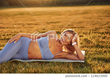 Resting on the ground. Beautiful woman in sportive clothes doing fitness exercises outdoors on the field Resting on the ground. Beautiful woman in sportive clothes doing fitness exercises outdoors on the field 124623000