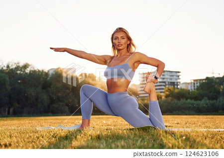 Against bright background. Beautiful woman in sportive clothes doing fitness exercises outdoors on the field Against bright background. Beautiful woman in sportive clothes doing fitness exercises outdoors on the field 124623106