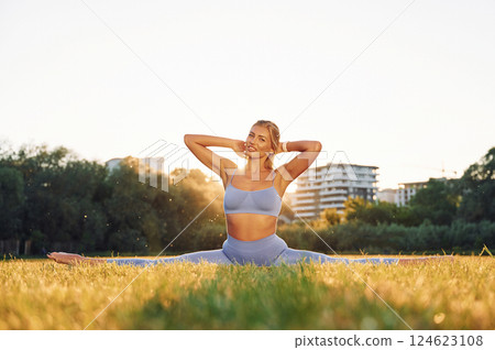 Against bright background. Beautiful woman in sportive clothes doing fitness exercises outdoors on the field 124623108