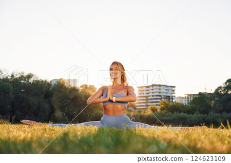 Stretching the legs. Beautiful woman in sportive clothes doing fitness exercises outdoors on the field Stretching the legs. Beautiful woman in sportive clothes doing fitness exercises outdoors on the field 124623109