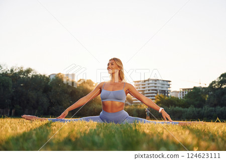 Stretching the legs. Beautiful woman in sportive clothes doing fitness exercises outdoors on the field Stretching the legs. Beautiful woman in sportive clothes doing fitness exercises outdoors on the field 124623111