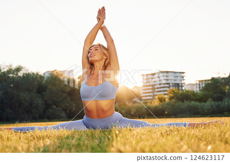 Flexible body. Beautiful woman in sportive clothes doing fitness exercises outdoors on the field Flexible body. Beautiful woman in sportive clothes doing fitness exercises outdoors on the field 124623117