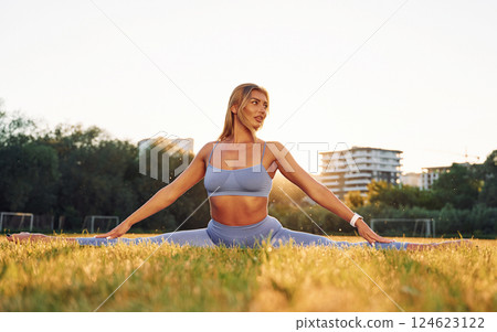 Flexible body. Beautiful woman in sportive clothes doing fitness exercises outdoors on the field 124623122