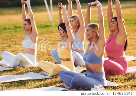 Stretching in lotus pose. Group of women have fitness outdoors on the field together 124623141