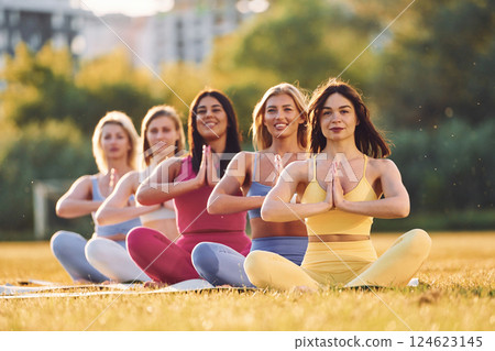 Calm meditation in lotus pose. Group of women have fitness outdoors on the field together Calm meditation in lotus pose. Group of women have fitness outdoors on the field together 124623145
