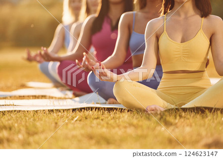 Calm meditation in lotus pose. Group of women have fitness outdoors on the field together Calm meditation in lotus pose. Group of women have fitness outdoors on the field together 124623147
