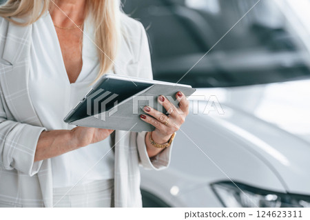 With notepad in hands. Woman in white formal clothes is in the car dealership 124623311