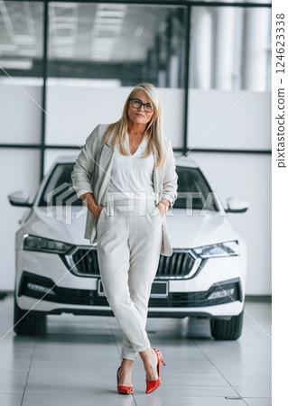 Standing and posing. Woman in white formal clothes is in the car dealership 124623338