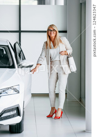 Going to the automobile. Woman in white formal clothes is in the car dealership 124623347