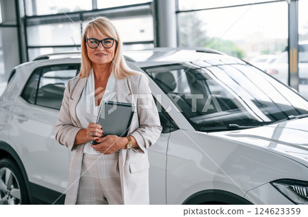 Manager with documents. Woman in white formal clothes is in the car dealership Manager with documents. Woman in white formal clothes is in the car dealership 124623359