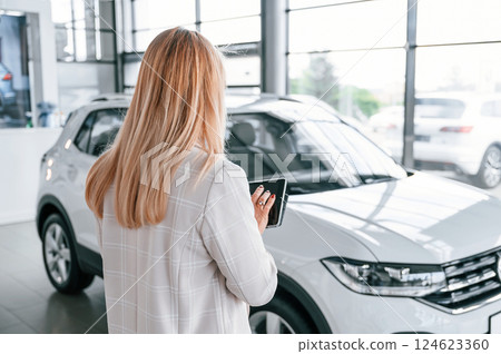 Manager with documents. Woman in white formal clothes is in the car dealership 124623360