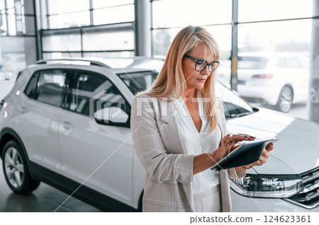 Manager with documents. Woman in white formal clothes is in the car dealership 124623361