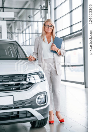 Manager is ready to help. Woman in white formal clothes is in the car dealership 124623366