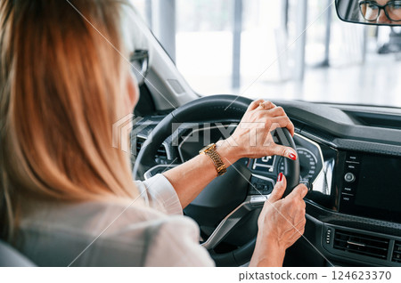 Sitting in the automobile. Woman in white formal clothes is in the car dealership Sitting in the automobile. Woman in white formal clothes is in the car dealership 124623370