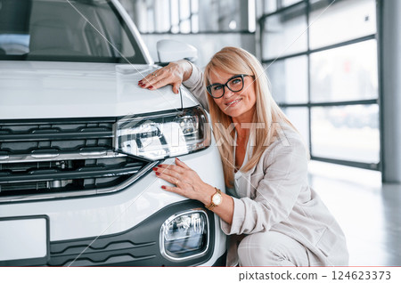 Embracing the car. Woman in white formal clothes is in the car dealership 124623373