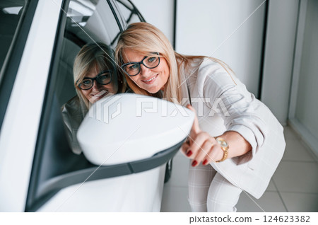 Looking into the side mirror. Woman in white formal clothes is in the car dealership 124623382