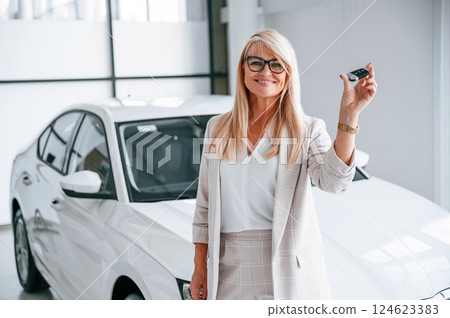Holding keys. Woman in white formal clothes is in the car dealership 124623383