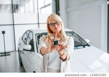 Holding keys. Woman in white formal clothes is in the car dealership Holding keys. Woman in white formal clothes is in the car dealership 124623385