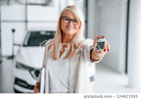 Automobile owner is holding keys. Woman in white formal clothes is in the car dealership 124623393