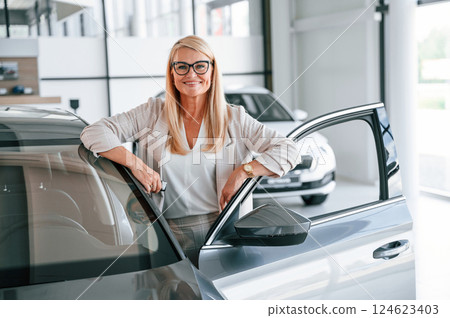 Happy positive woman in white formal clothes is in the car dealership Happy positive woman in white formal clothes is in the car dealership 124623403
