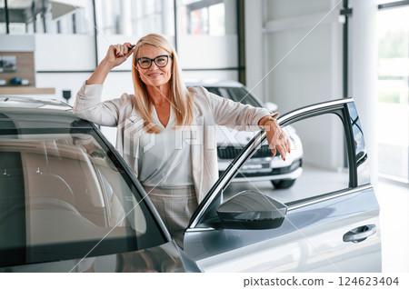 Happy positive woman in white formal clothes is in the car dealership 124623404