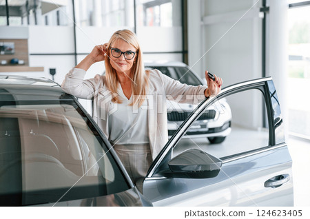 Happy positive woman in white formal clothes is in the car dealership 124623405