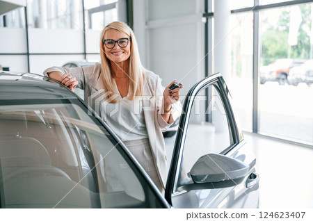 Happy positive woman in white formal clothes is in the car dealership 124623407