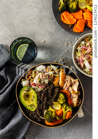 A hearty, balanced breakfast bowl with black quinoa, creamy avocado, roast chicken, sweet potatoes, zucchini, broccoli, and a fresh salad of cabbage and radish with chia and sesame seeds 124623412