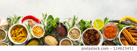Assorted cooking spices and herbs arranged on a gray surface, featuring natural tones that add depth and aroma to any meal, banner 124623451