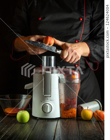 A chef prepares juicy apples with an electric juicer in a dark kitchen. Colourful apples surround the machine, ready to be turned into a refreshing drink 124624084